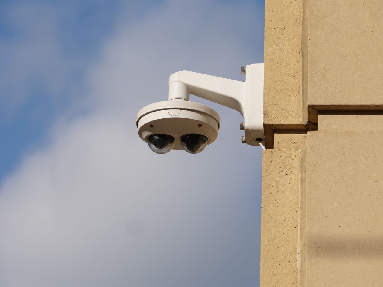 Modern security camera on an urban building wall against a blue sky.